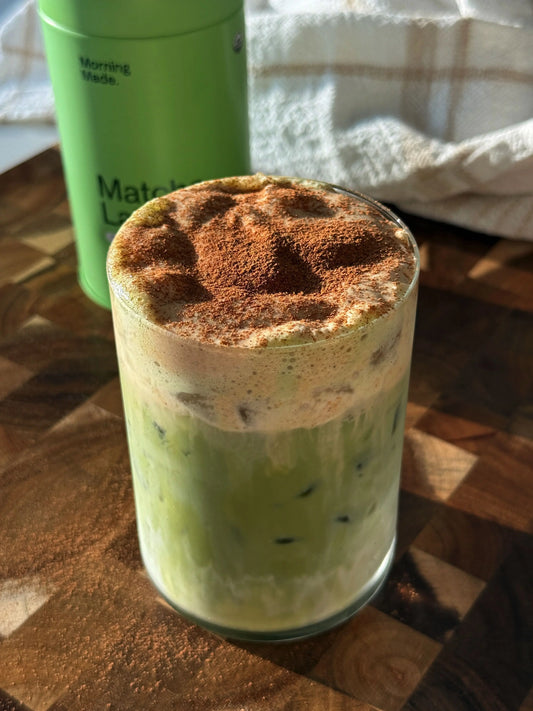 Image of glass of Pumpkin Cream Matcha Latte sitting on a wooden benchtop.